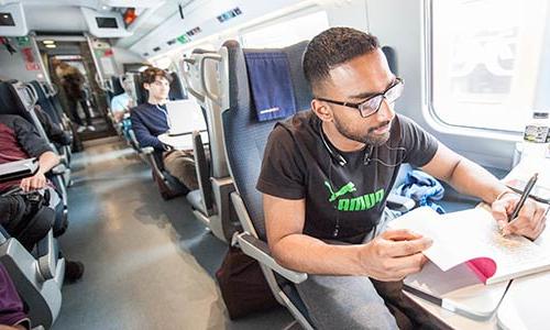 Male student writing a reflection on a train