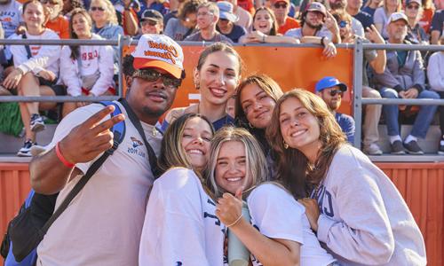 A group of young people smiling and posing together at what appears to be a sports stadium or arena. 